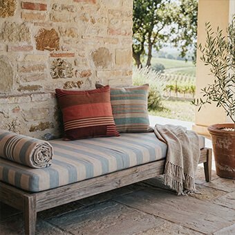 Custom-made outdoor bench cushions with blue stripes and decorative terracotta and teal pillows on a rustic wooden daybed, crafted by WM Design Furniture in Van Nuys.