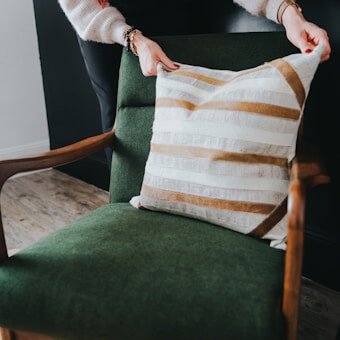 Hand placing a custom-made striped outdoor cushion on a green vintage-style chair, handcrafted by WM Design Furniture in Van Nuys