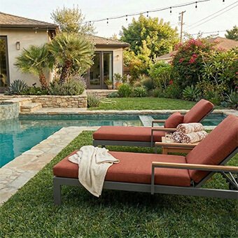 Pair of modern outdoor lounge chairs with custom terracotta solid-colored cushions by a luxury pool and green lawn, manufactured by WM Design Furniture in Van Nuys.