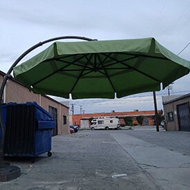 Large green cantilever patio umbrella undergoing professional maintenance and cleaning in Van Nuys.