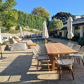Ivory outdoor dining chair seat cushions around a wooden table and matching ivory chaise lounge pads by a pool in a Los Angeles backyard.