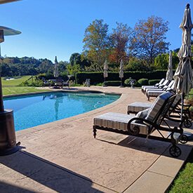 Luxury pool lounge chairs with custom striped cushions and patio umbrellas in a Van Nuys residential estate.