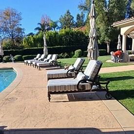 Neutral striped outdoor chaise lounge cushions on dark wrought iron wheeled pool chairs in a Los Angeles luxury backyard.