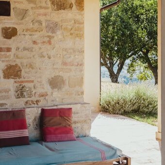A rustic stone courtyard seating area with custom-fitted deep red and teal striped patio bench cushions and decorative pillows by WM Design Furniture Van Nuys.