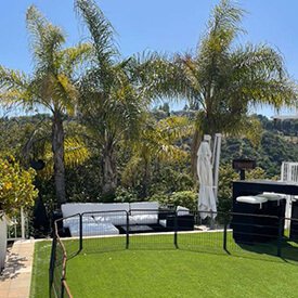 White outdoor sectional cushions with matching ottoman and bar stool pads on a modern terrace with artificial grass in Los Angeles.